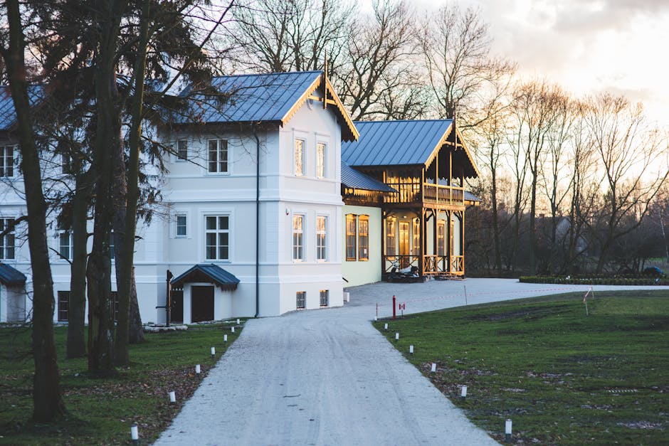 White mansion with a garden and driveway at sunset, showcasing elegant architecture