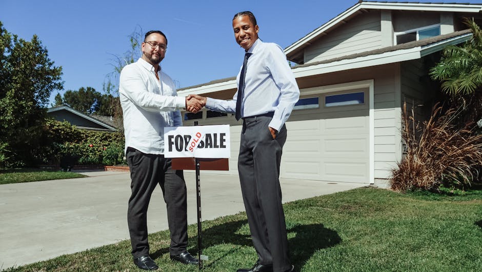 Two men shake hands in front of a new home with a sold sign